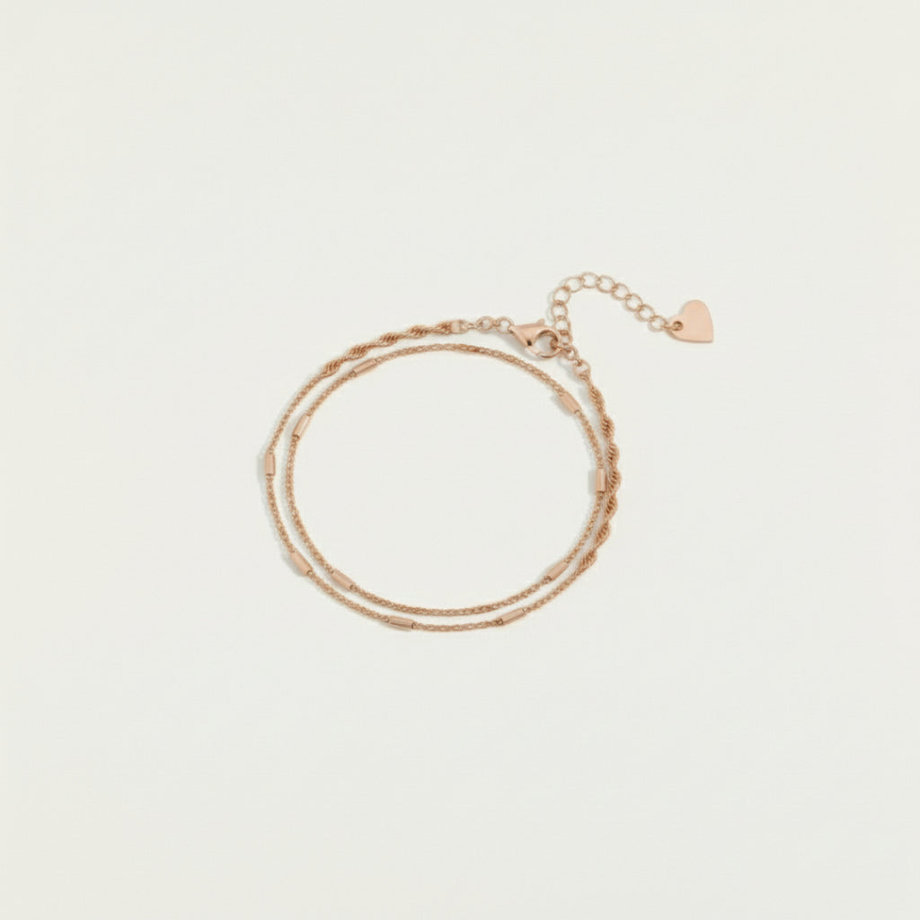 Top view of the Minimalist Double Bracelet Set in rose gold featuring dual delicate chains with heart clasp and adjustable link, displayed on a soft off-white #F0EDE7 background in luxury jewelry style.