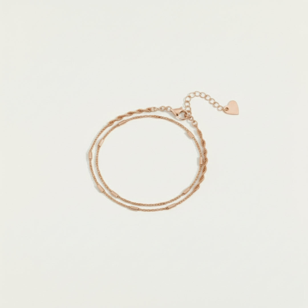 Top view of the Minimalist Double Bracelet Set in rose gold featuring dual delicate chains with heart clasp and adjustable link, displayed on a soft off-white #F0EDE7 background in luxury jewelry style.
