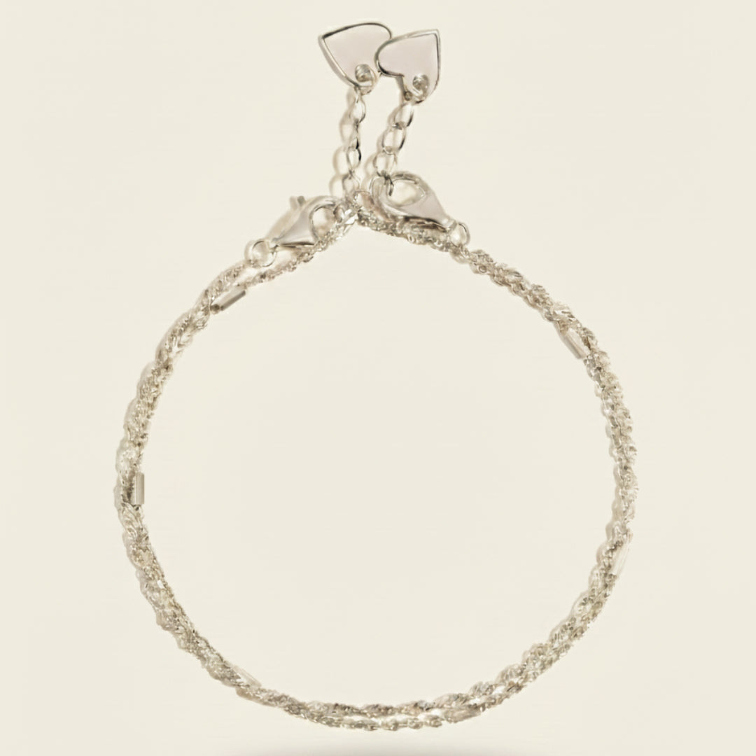 Minimalist double bracelet set in sterling silver featuring a braided chain design with dual heart clasps, displayed on a soft off-white #F0EDE7 background in luxury jewelry photography style.